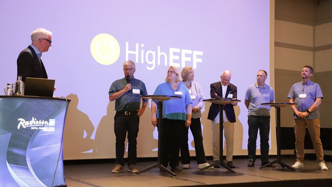 People on a stage, participating in a debate, with the logo of the HighEFF research centre on a screen behind them.