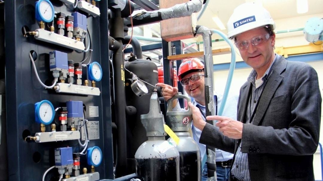 To personer med vernebriller og hjelmer, én med SINTEF-logo, står ved et teknisk anlegg med måleinstrumenter og ventiler.